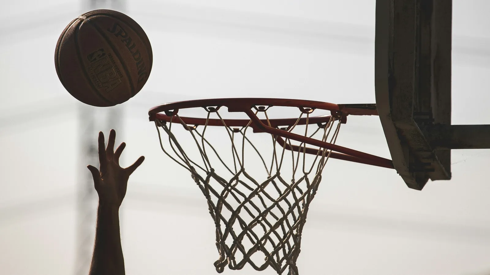 Ballon lancé vers un panier de basket, en contre-jour