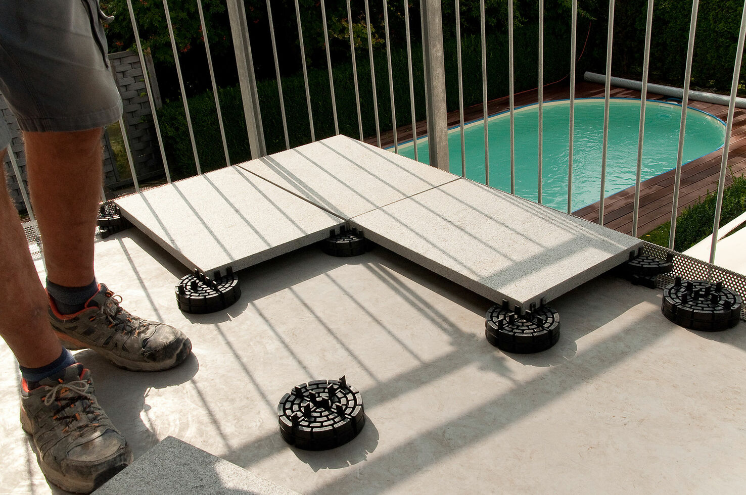 Handwerker verlegt großformatige Terrassenplatten auf PLATTENFIX Stelzlagern neben einem Pool
