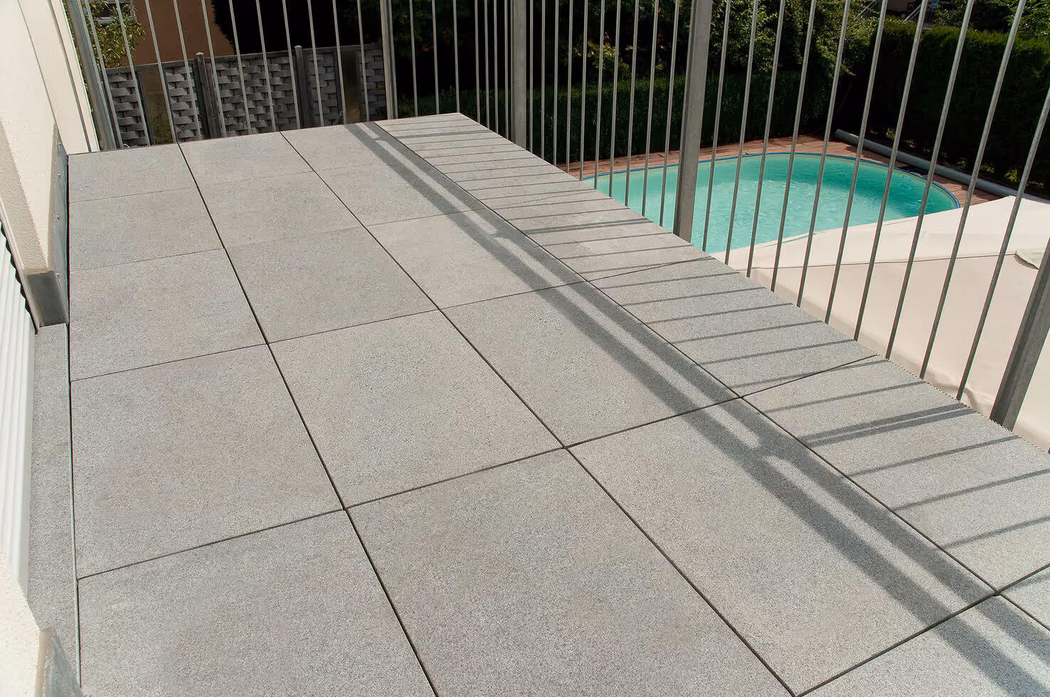 Balcony with large gray square tiles and metal railing overlooking a backyard pool.