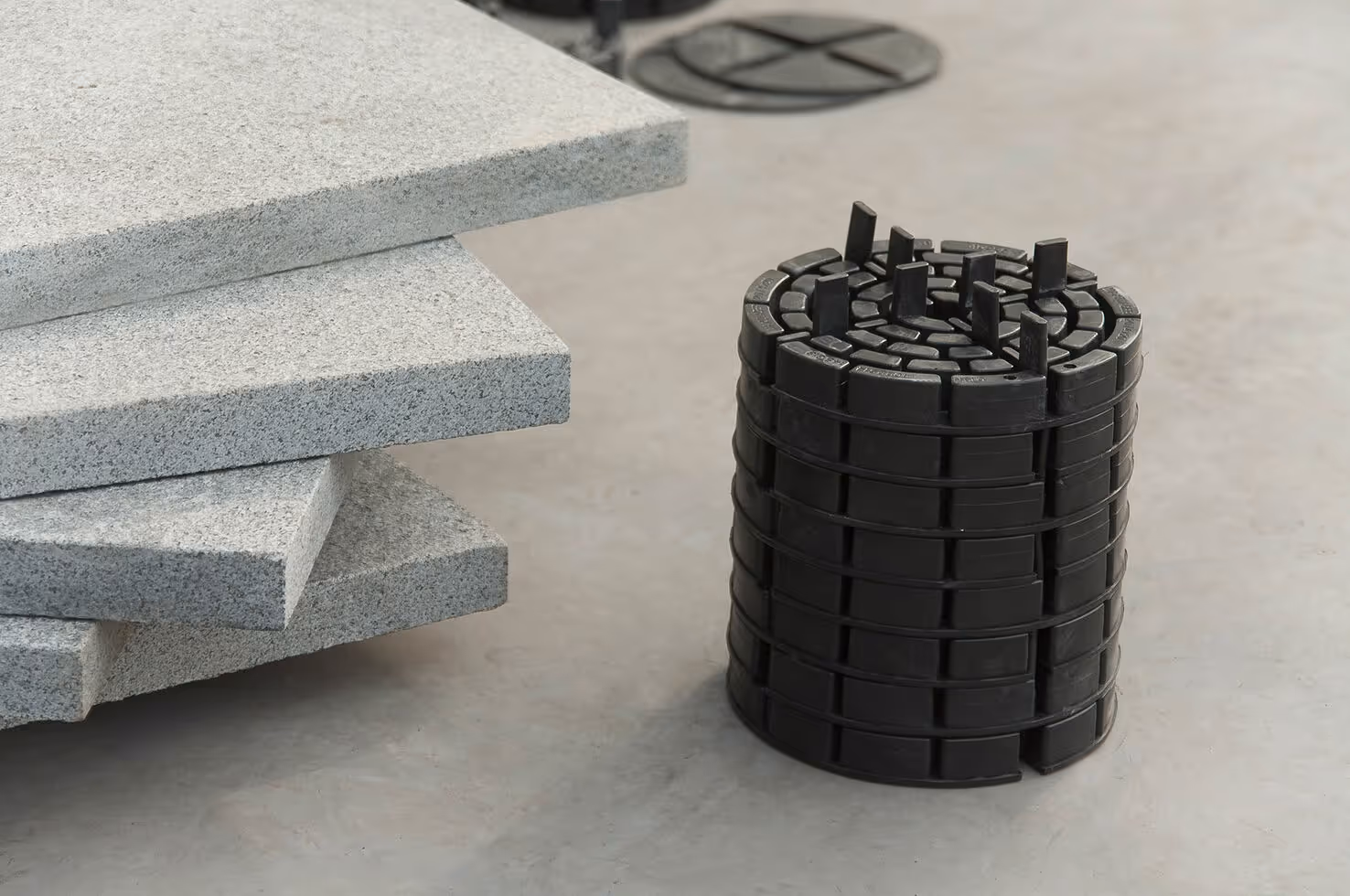 Gestapelte Natursteinplatten neben einem PLATTENFIX MULTI Stelzlager auf einer Betonfläche