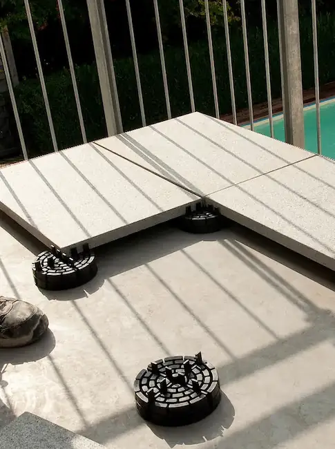 PLATTENFIX Stelzlager unter großformatigen Terrassenplatten am Pool verlegt, mit Metallgeländer im Hintergrund