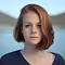 Portrait of a woman with short red hair against a blurred outdoor background.
