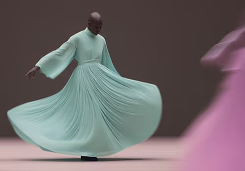 Person spinning in a flowing, pleated light green dress on a neutral background.