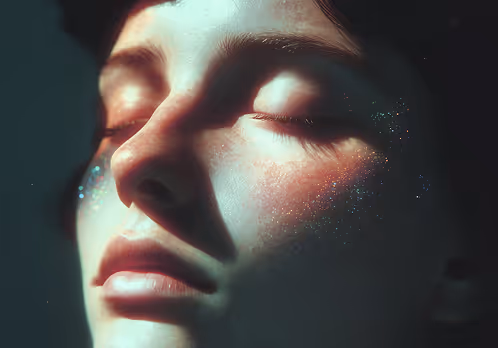 Close-up of a person’s face with eyes closed and glitter on cheeks, lit softly.
