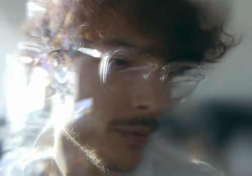 Blurred portrait of a person wearing clear glasses with light reflections around the face.