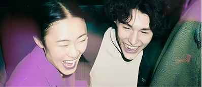 Two people laughing joyfully in close-up, with one wearing purple and the other black and white.