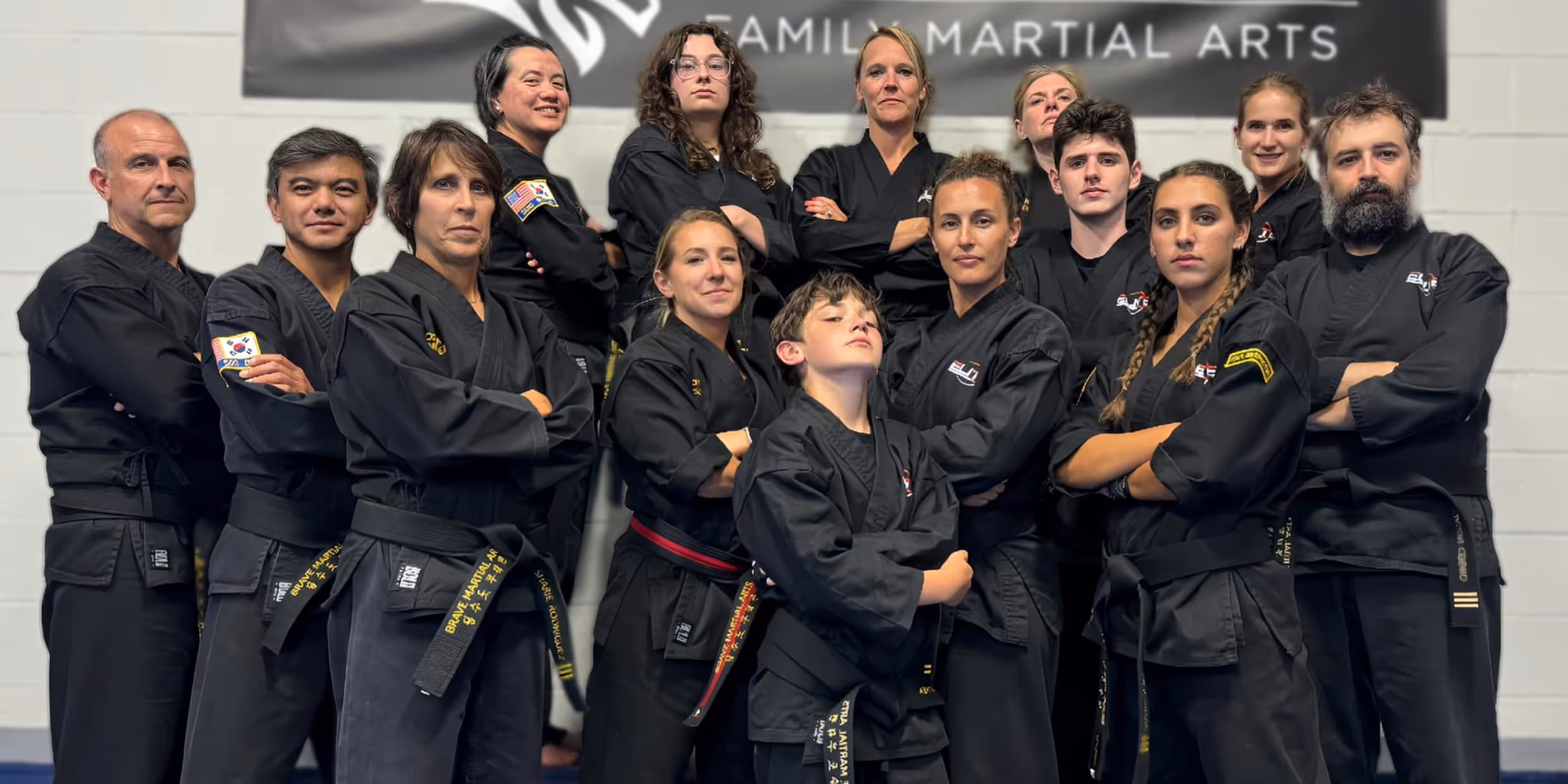 A diverse martial arts group poses confidently in black uniforms, showcasing unity and strength in front of a dojo banner.