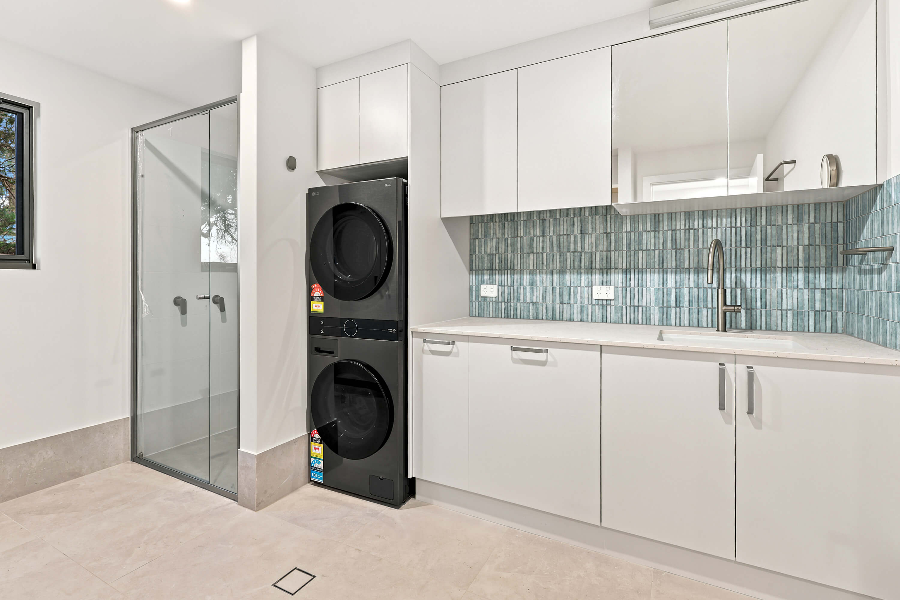 Laundry with stacked washer and dryer, blue mosaic splashback and glazed shower at Franklin Ave, Encounter Bay