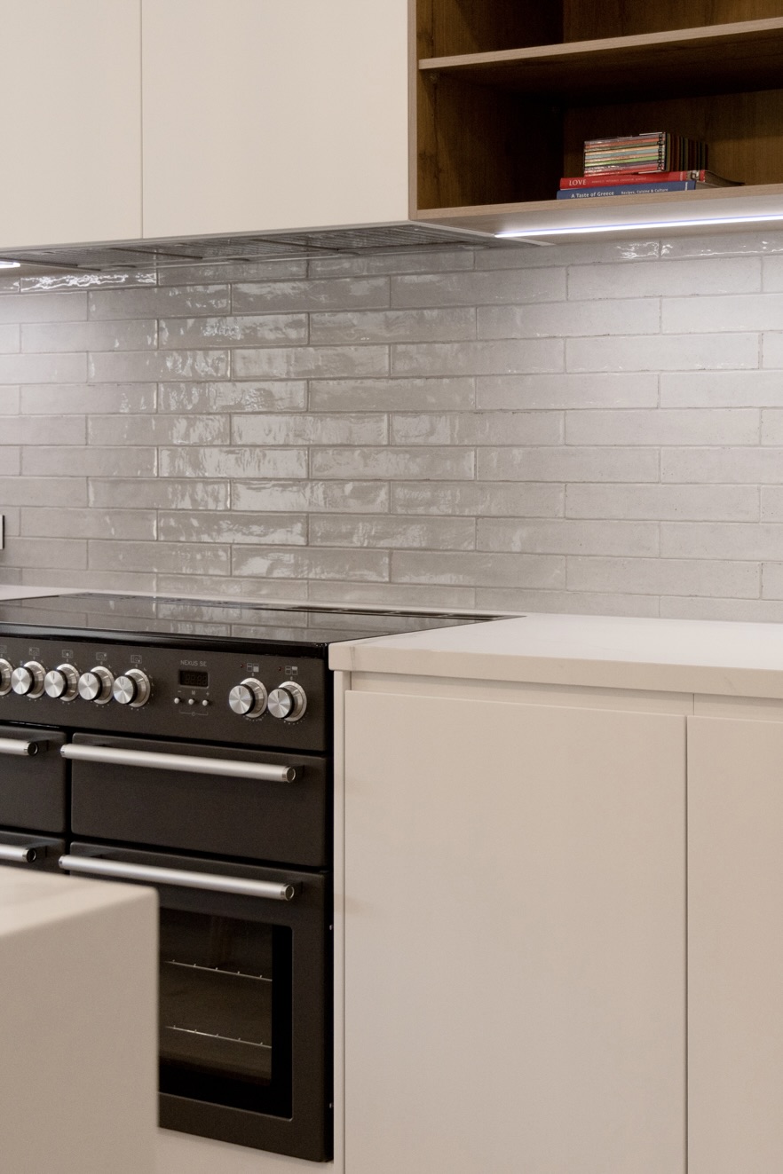 Black range cooker under glossy white subway tiles and oak shelving at Henry St, Port Elliot