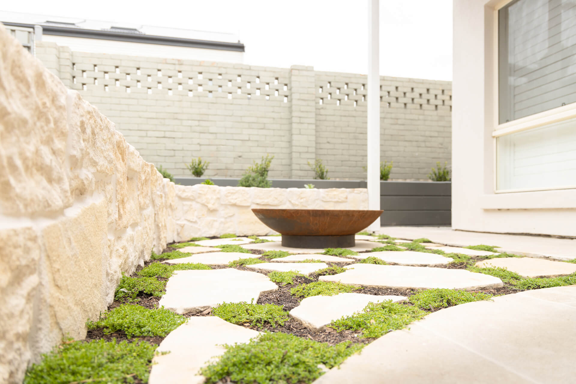 Limestone crazy paving with creeping groundcover and rusted steel fire bowl at Henry St, Port Elliot