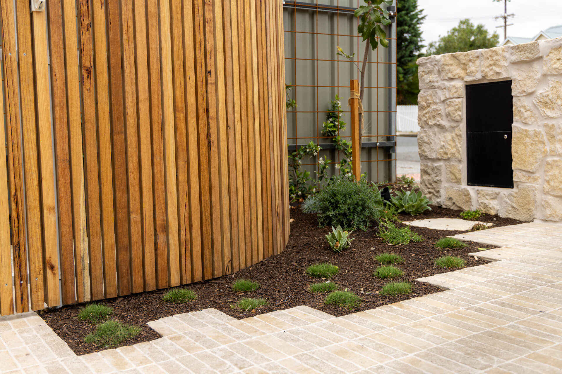 Spotted gum batten screen meeting limestone paving and mulched garden beds at Henry St, Port Elliot