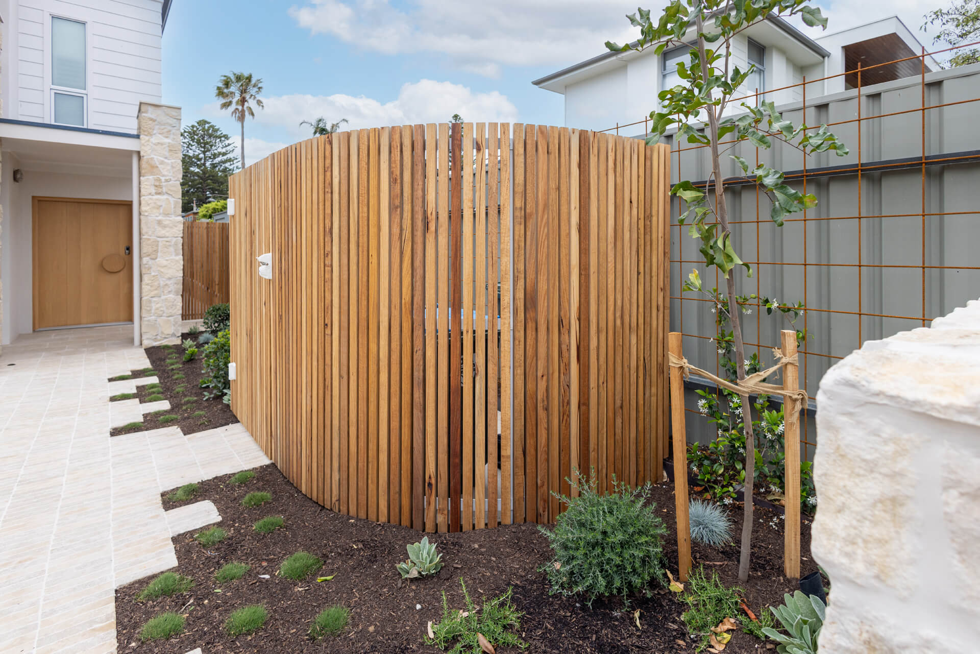 Curved spotted gum batten screen beside limestone paving and new garden beds at Henry St, Port Elliot