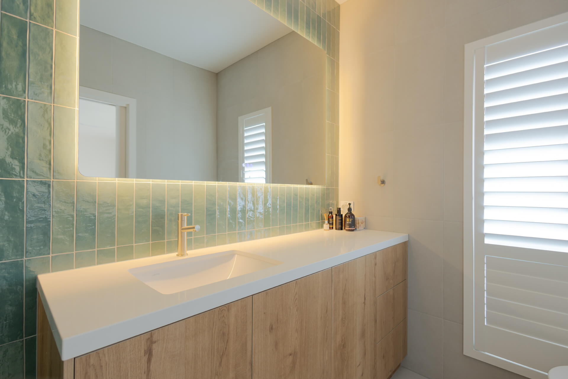 Ensuite with sea green feature tiles, brushed brass tapware and backlit mirror at Henry St, Port Elliot