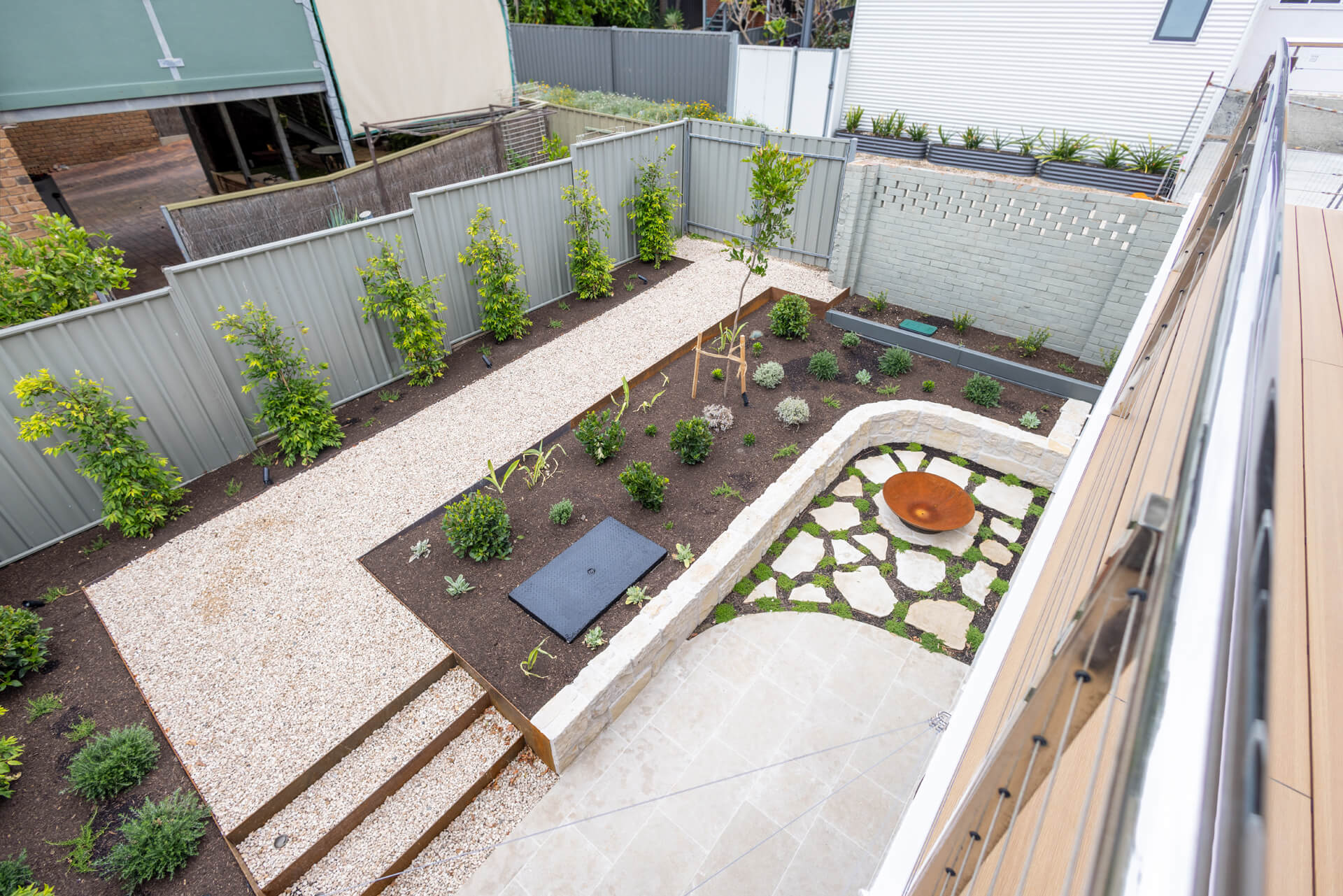 Elevated view over the Henry St backyard with gravel paths, young trees and limestone retaining, Port Elliot
