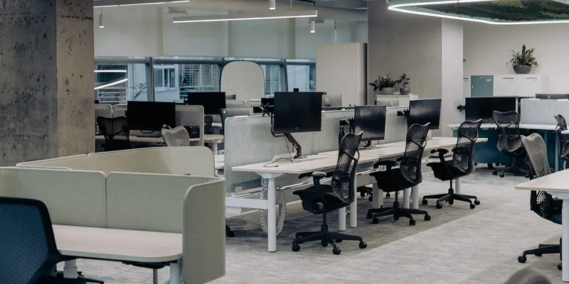 Modernes Büro mit mehreren leeren Schreibtischen, Computermonitoren und Bürostühlen in Reihen.