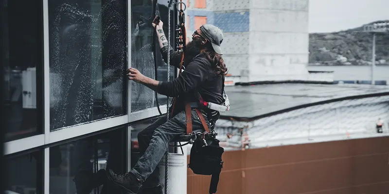 Fensterputzer mit Kletterausrüstung reinigt Fenster an einem Gebäude in großer Höhe.