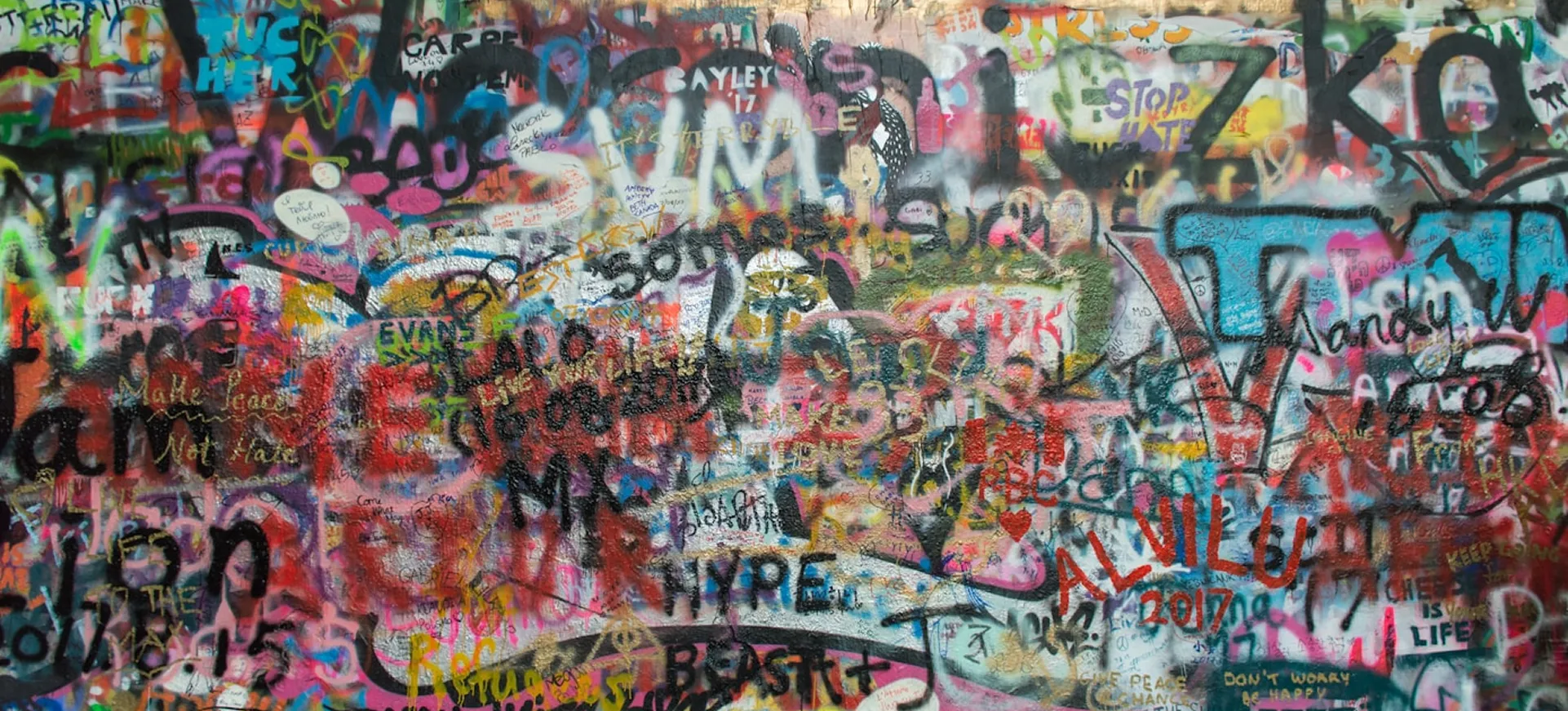 Bunte Wand mit dichter Graffiti-Schrift und Zeichnungen in vielen Farben und Stilen.