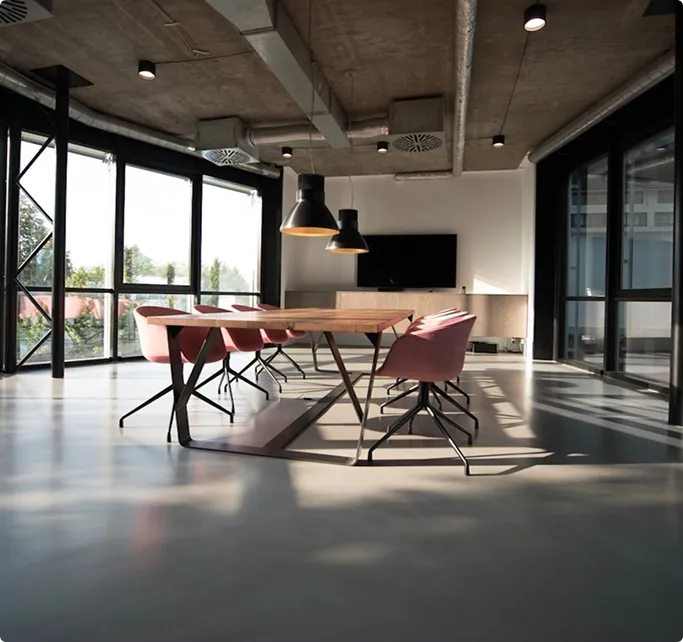 Modernes Büro mit großem Holztisch, sechs roten Stühlen und großen Fenstern mit Tageslicht.