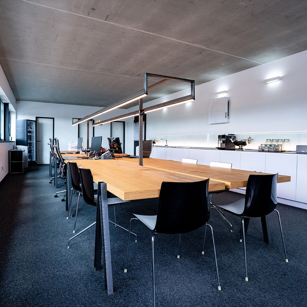 Heller Arbeitsraum mit langem Holztisch, Bürostühlen und Kaffeemaschine