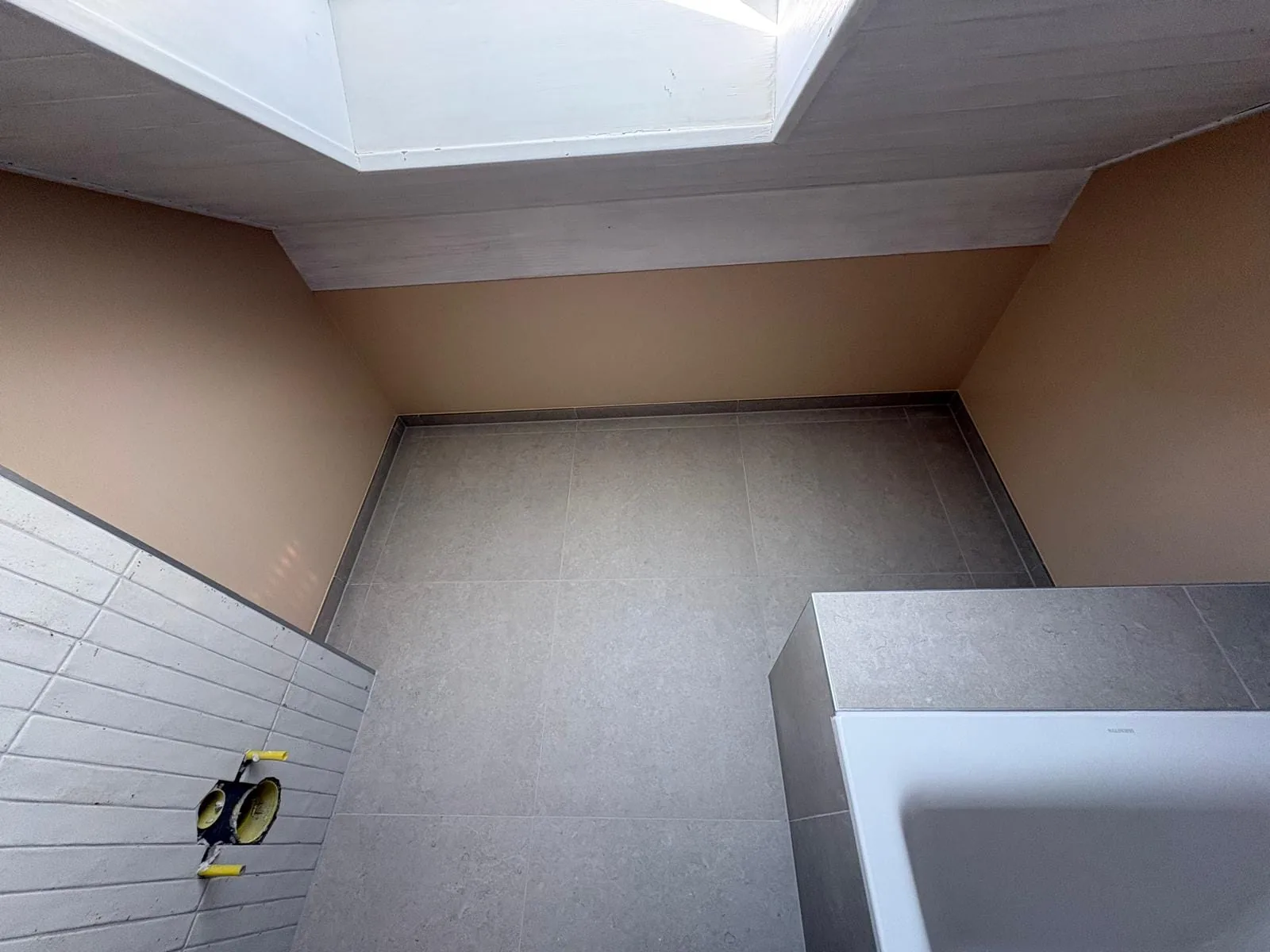Sol carrelé et plafond sous pente avec fenêtre de toit dans une salle de bain à Trélex