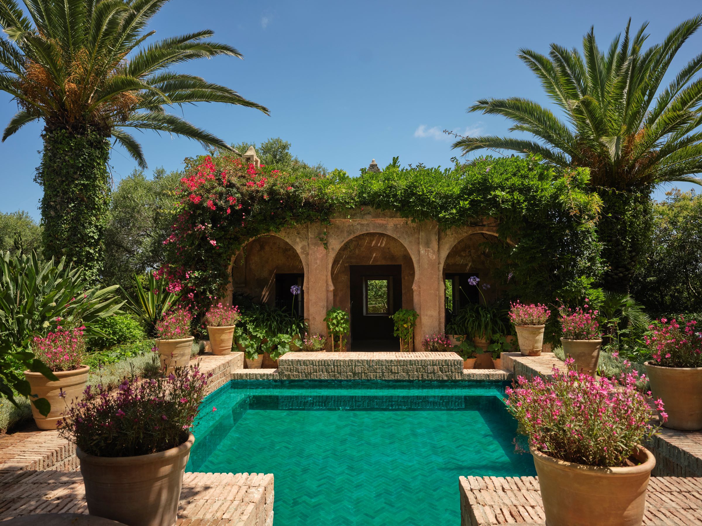 Turquoise swimming pool surrounded by palms and arches in the gardens of Villa Mabrouka