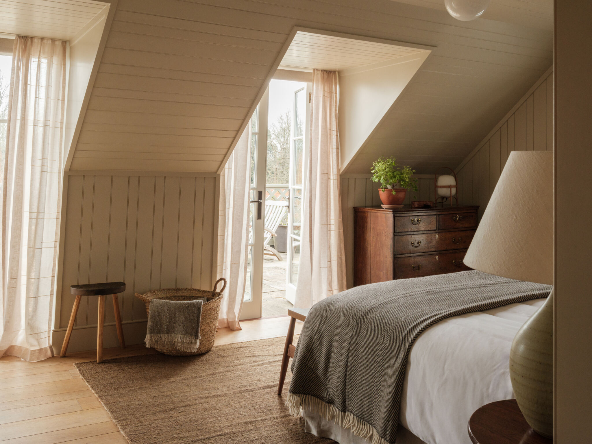 Bedroom under a sloping panelled ceiling with an antique chest of drawers at Heckfield Place