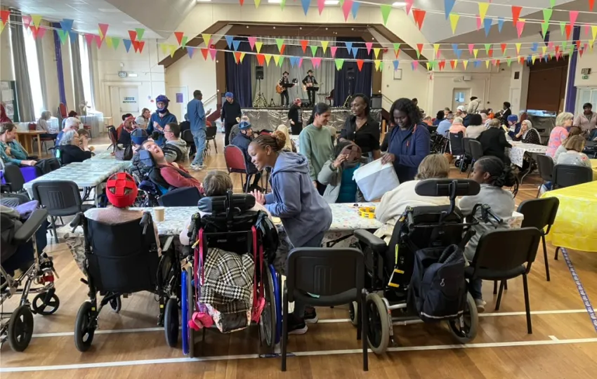 Community event in a hall with people, some in wheelchairs, socializing under colorful bunting flags.