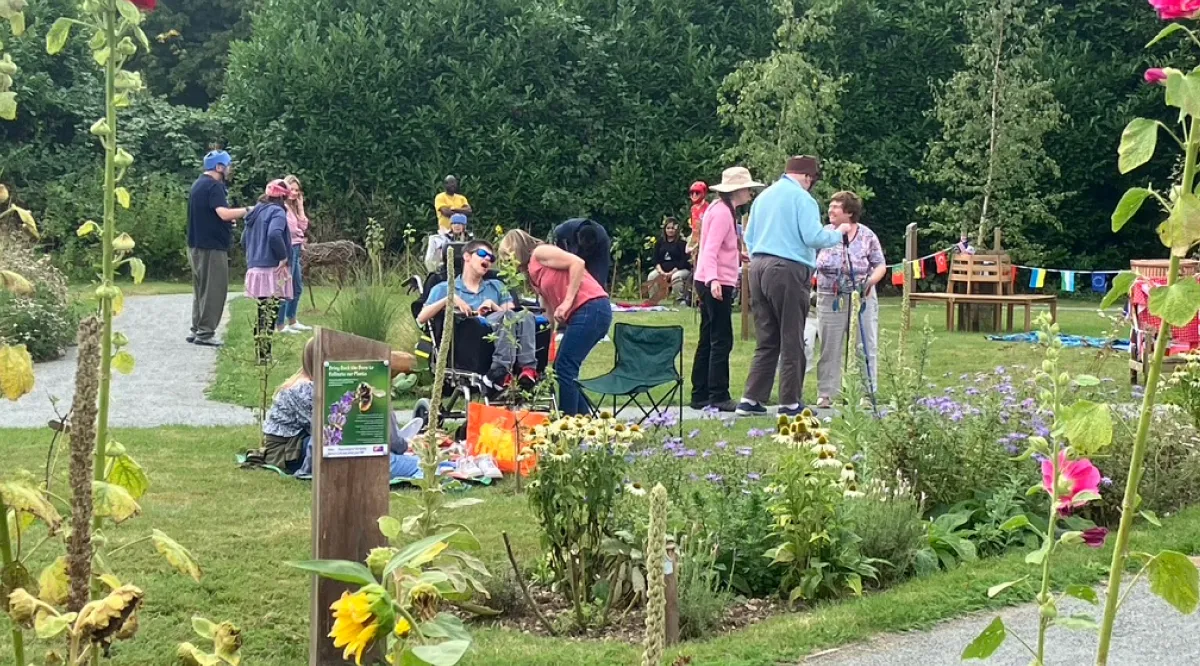 Group of people socialising and relaxing in a garden with colorful flowers and greenery.