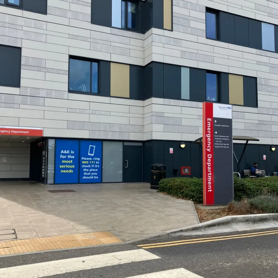Hospital emergency department entrance with signage advising to call NHS 111 for serious needs.
