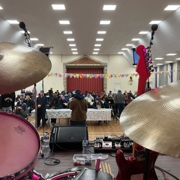 View from a stage with drums and guitar looking out at seated audience in a decorated hall.