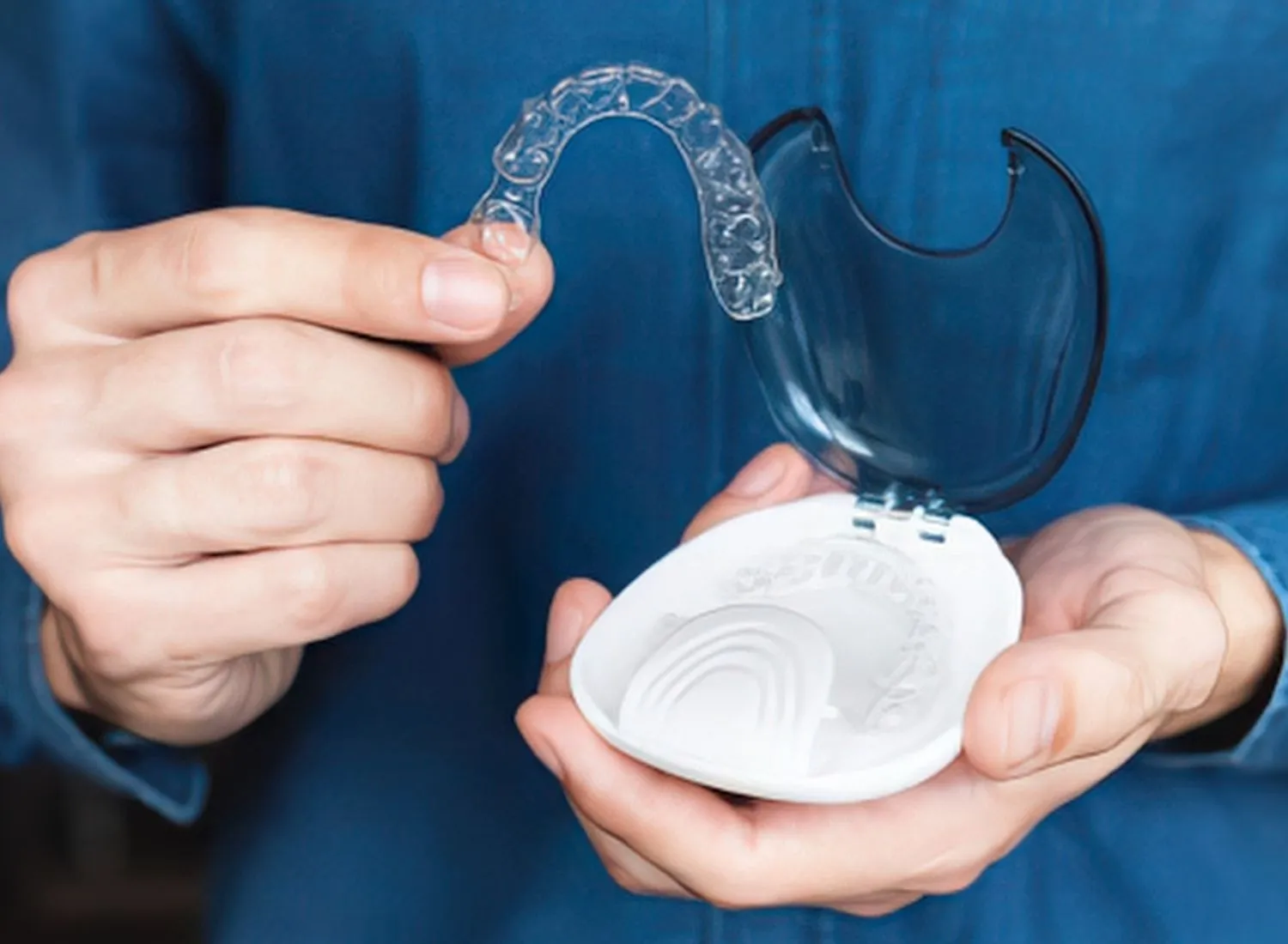 Person holding a clear dental night guard and its white plastic storage case with a dark lid.
