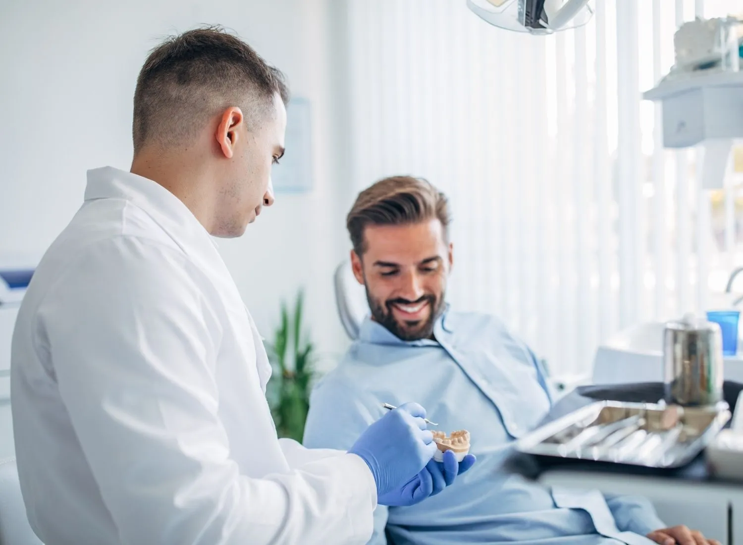 Dentist showing a dental mold to a smiling male patient in a bright dental office.