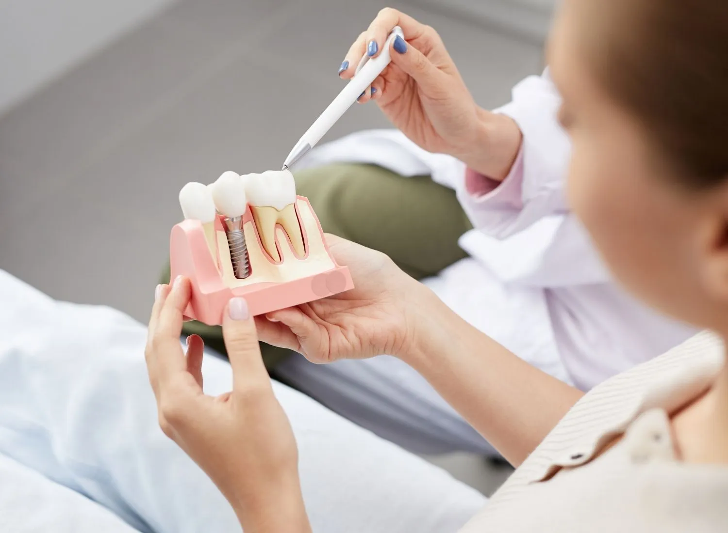 Person holding a dental model showing teeth and an implant with a dental professional pointing at it.