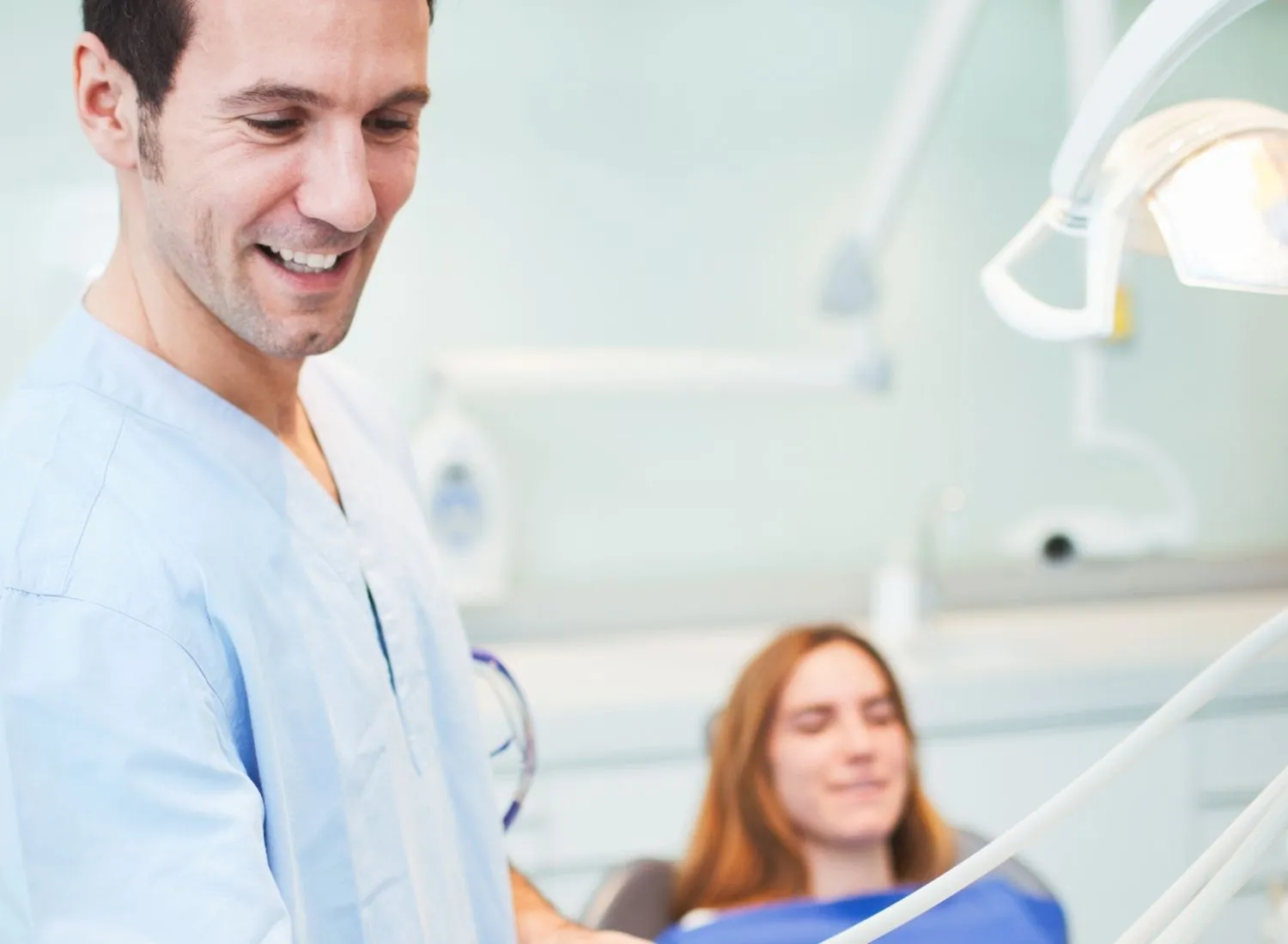 Male dentist smiling with a young female patient reclining in a dental chair.