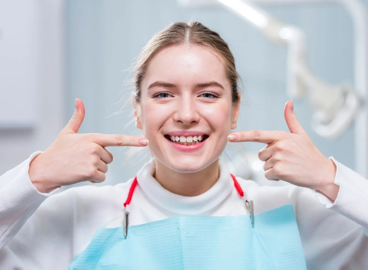Smiling woman in dental bib pointing at her teeth in a dental office.