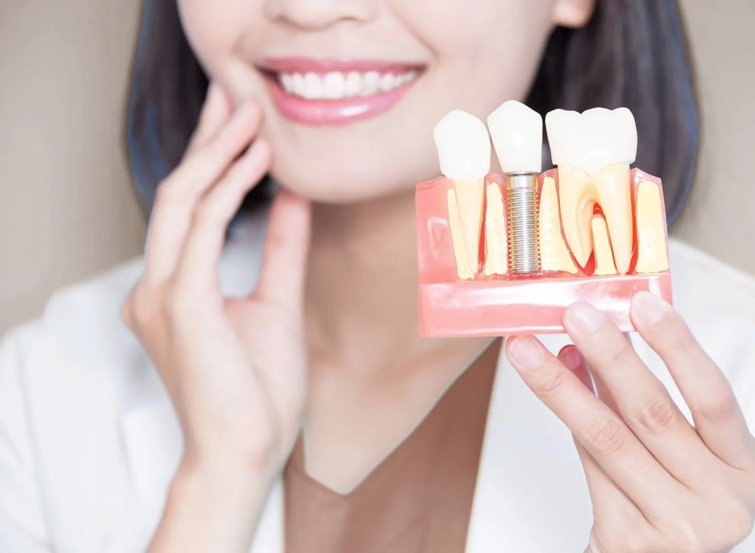 Smiling person holding a dental model showing a dental implant and natural teeth.