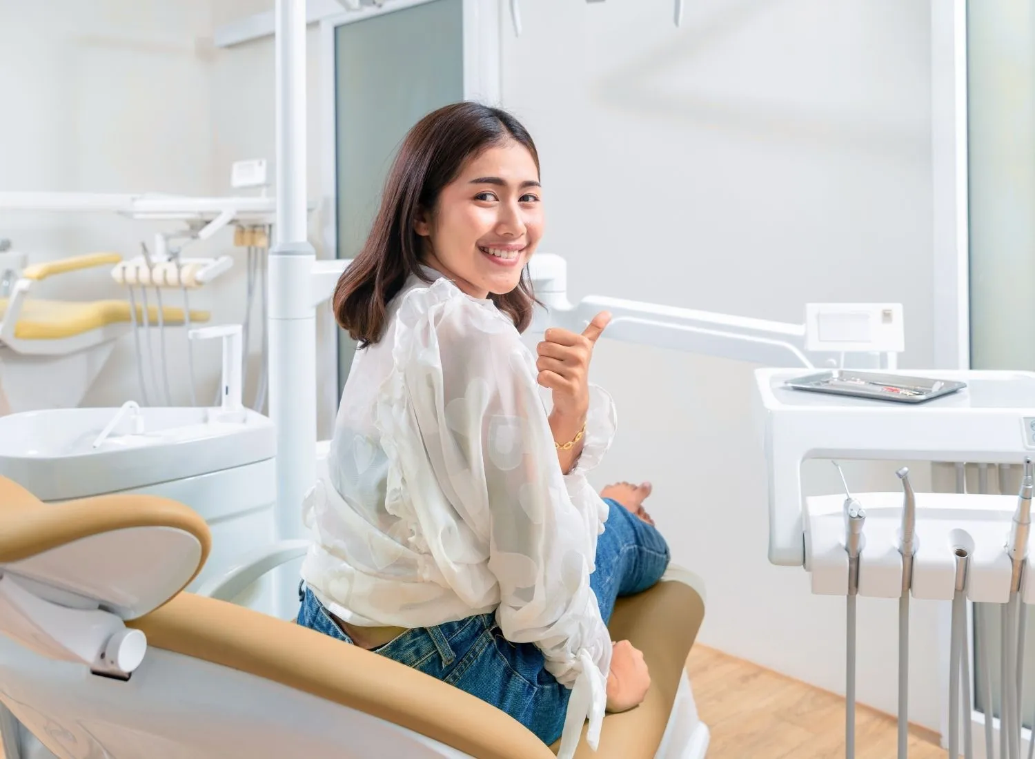 Smiling woman giving thumbs up sitting in a dental chair in a modern dental clinic.
