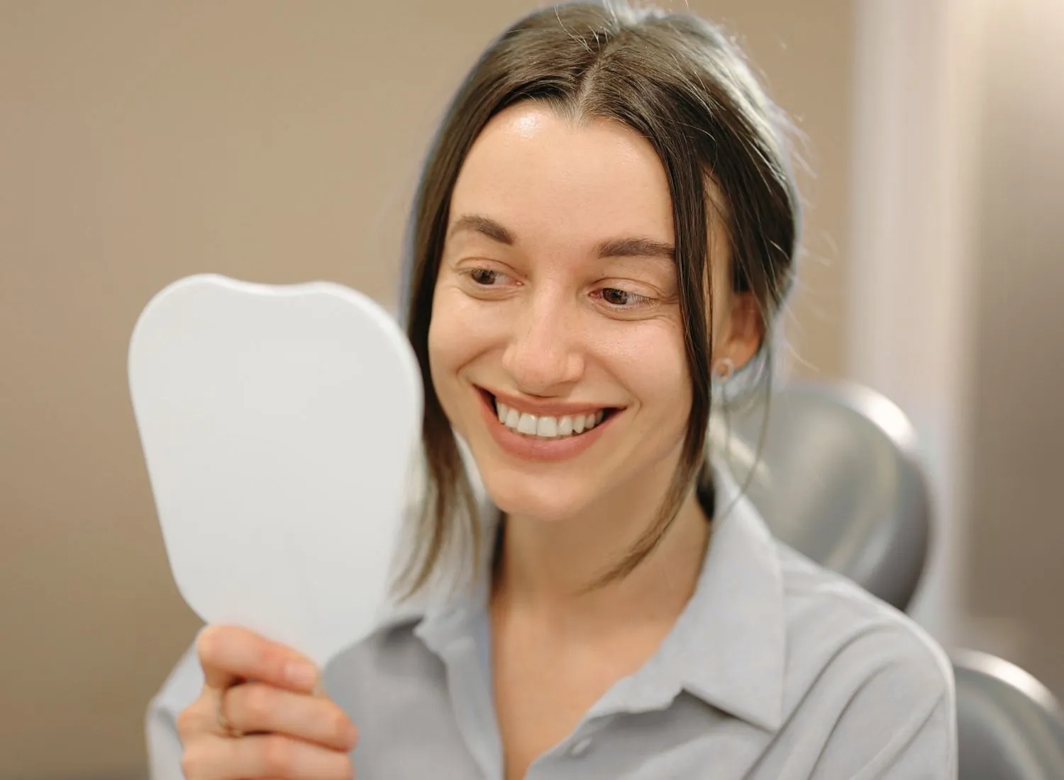 Smiling woman looking at her reflection in a tooth-shaped mirror at a dental office.