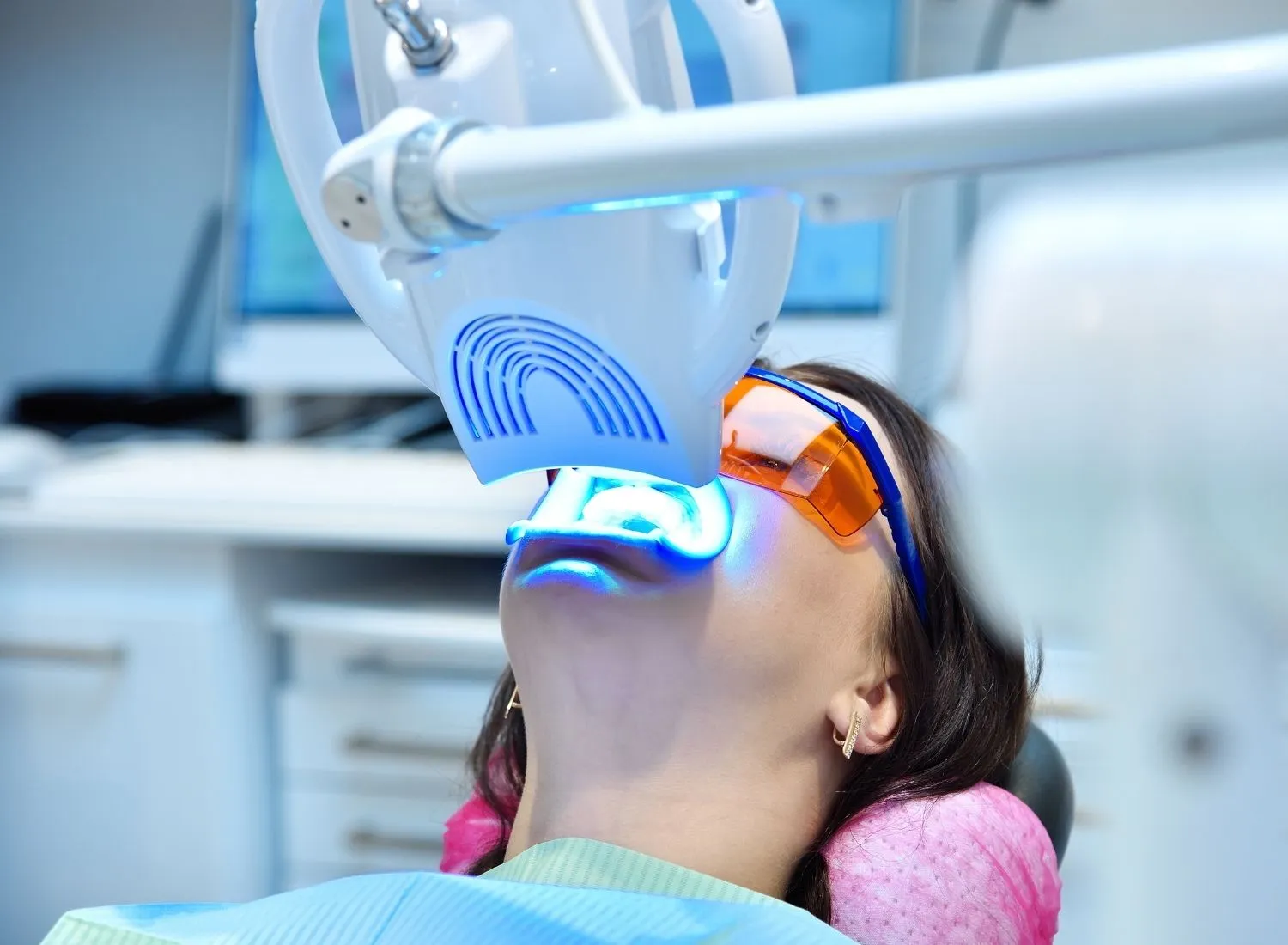 Patient wearing protective goggles undergoing blue light teeth whitening treatment in dental chair.