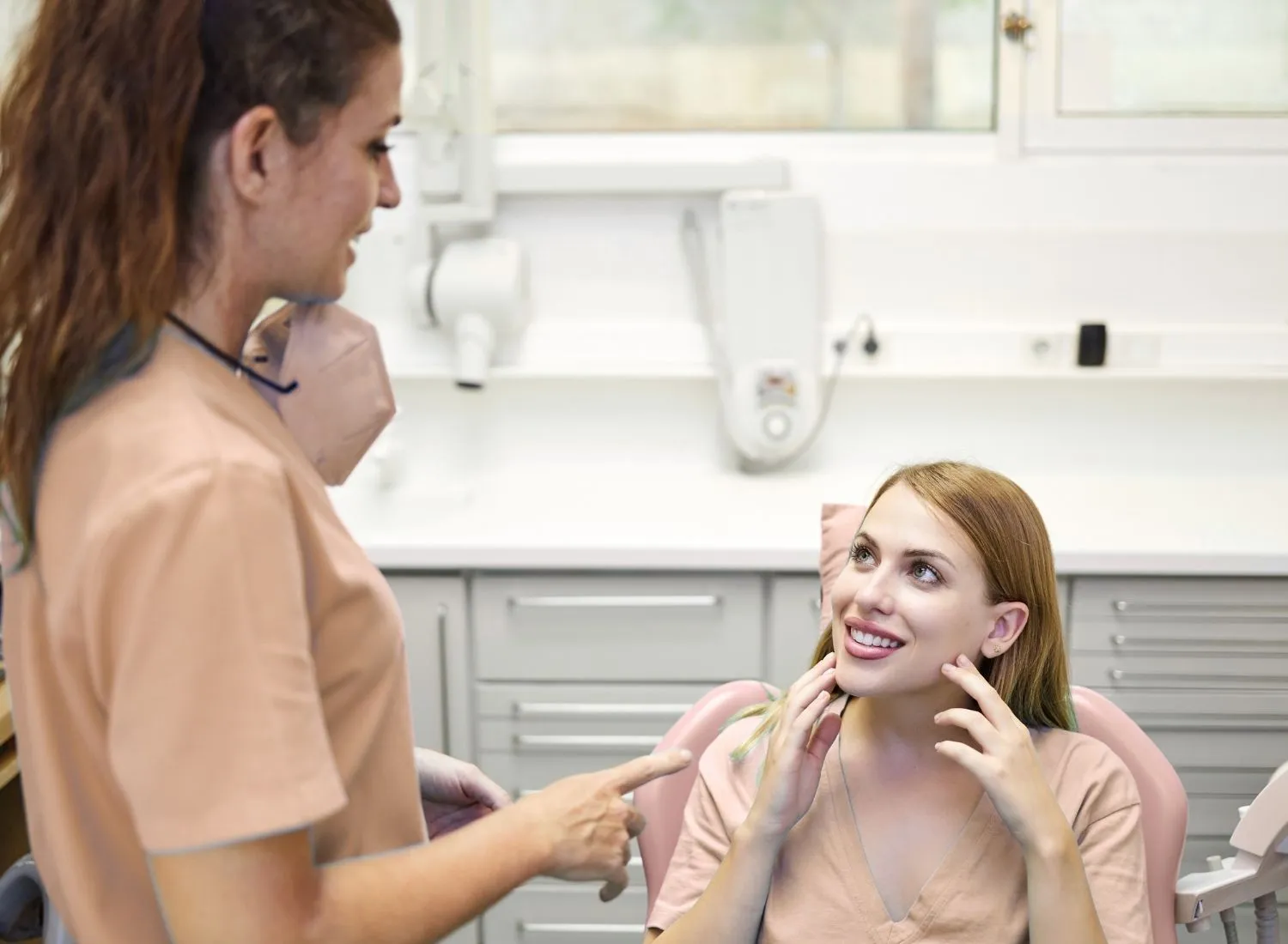 Dentist consulting a smiling female patient sitting in a dental chair in a clinic.
