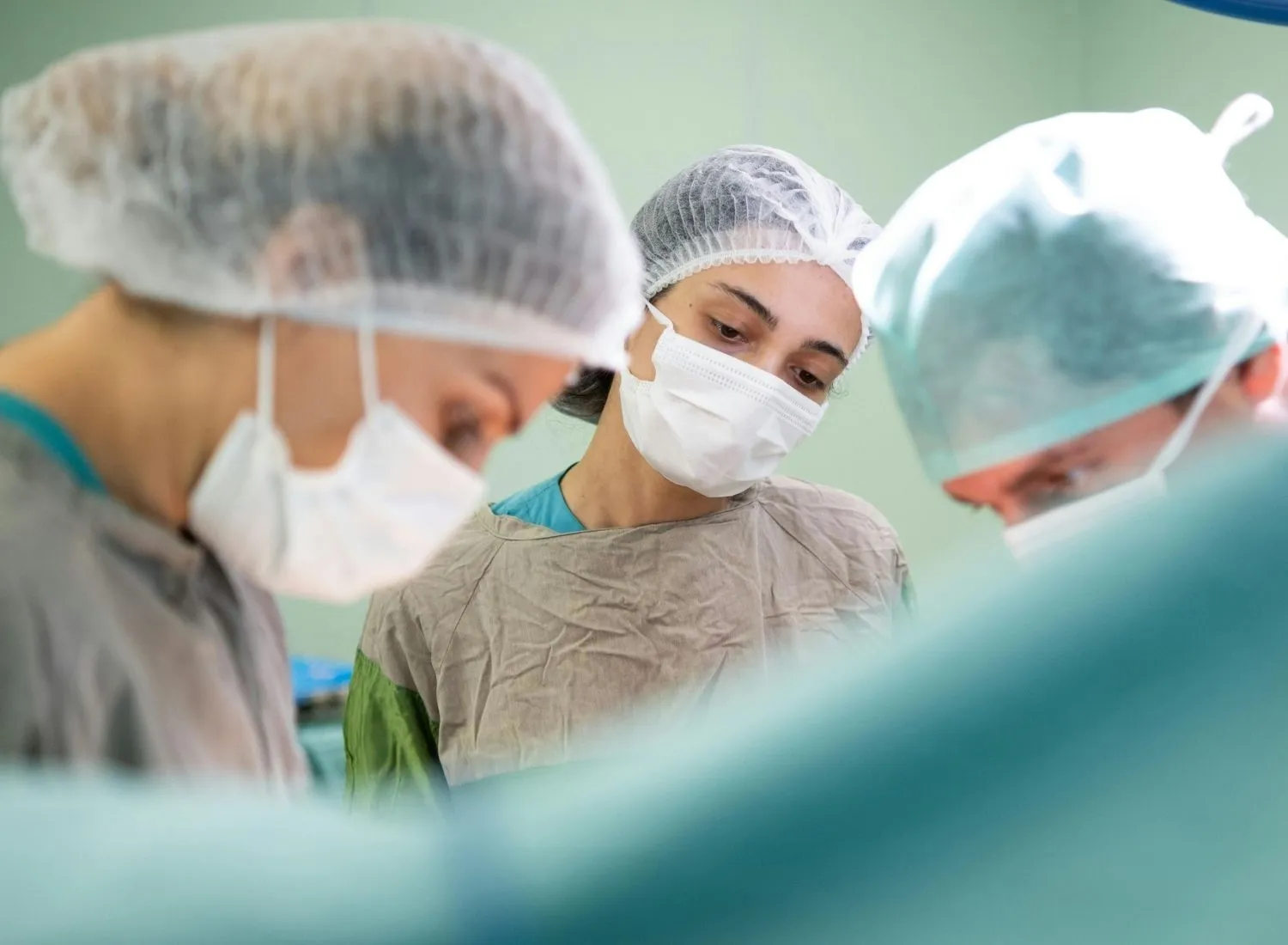 Three medical professionals wearing surgical caps and masks focusing on a task in a clinical setting.