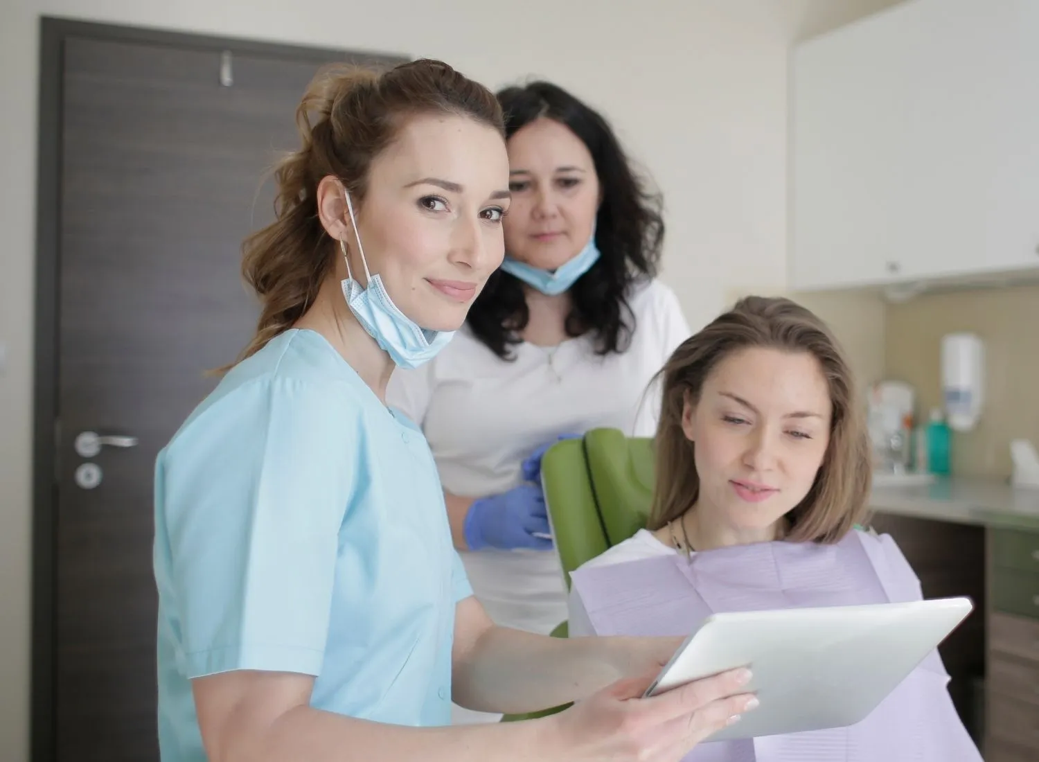 Female dentist in scrubs shows a tablet to a seated female patient at a dental office.