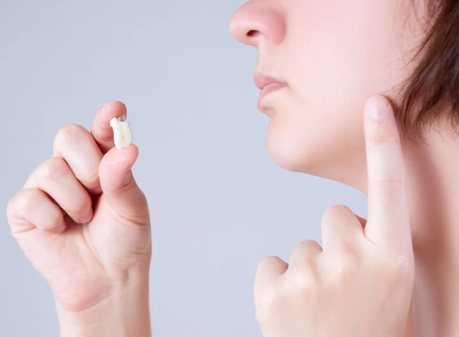 Person holding an extracted tooth while pointing to their jaw with the other hand.
