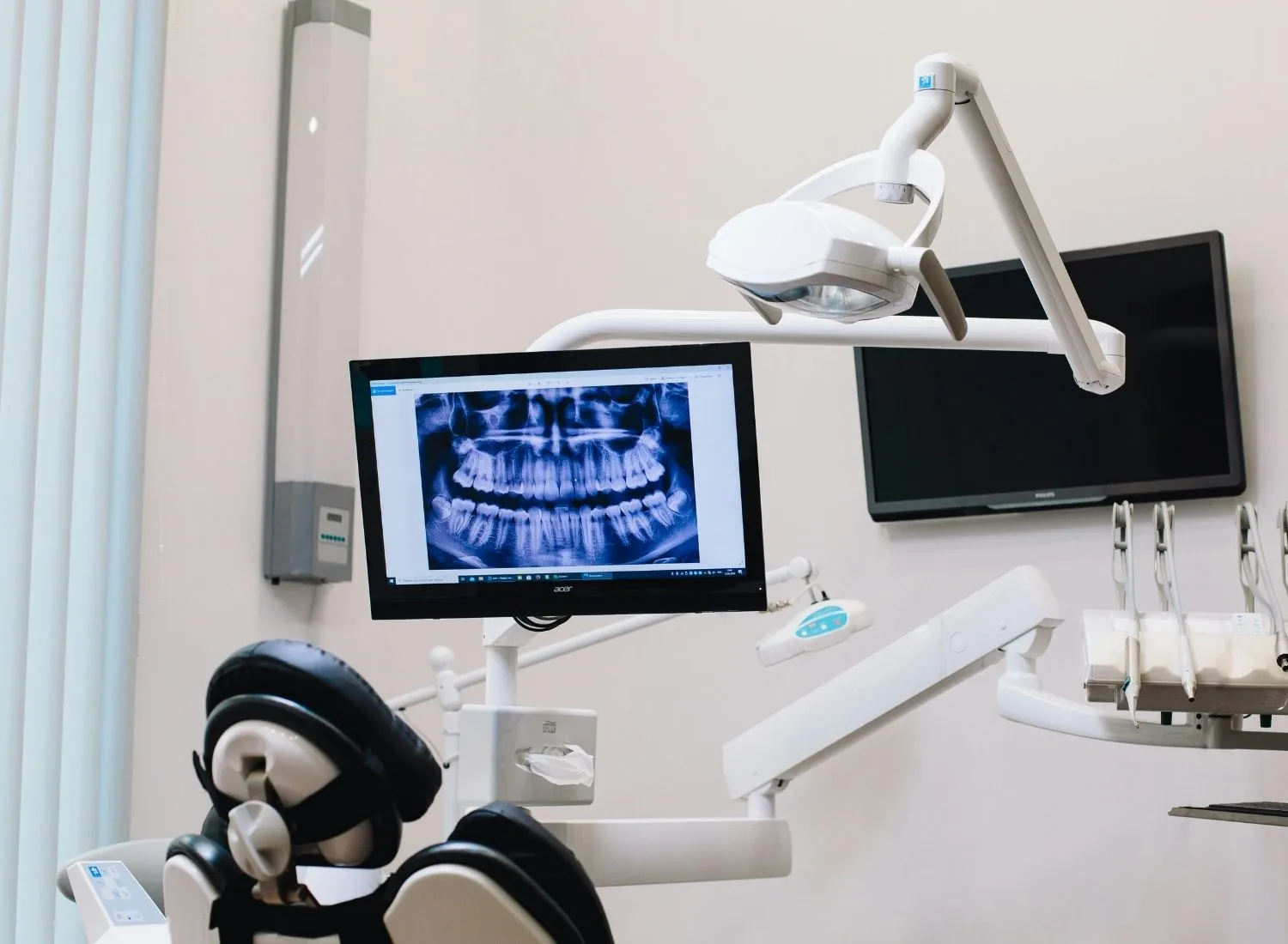 Dental clinic setup showing a patient chair with attached equipment and X-ray of teeth on a monitor.