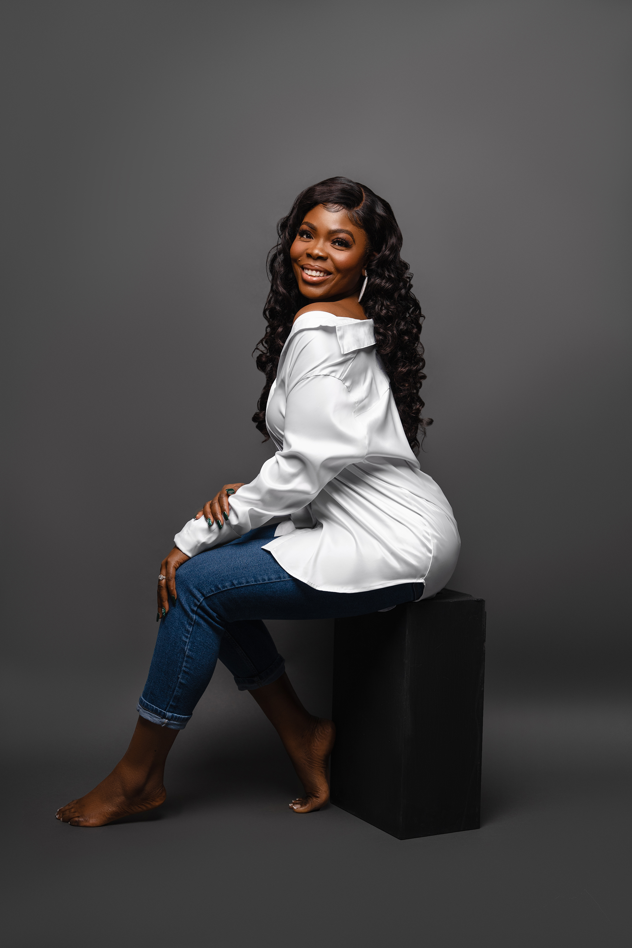 Full-length studio portrait of a Black woman in a white shirt and jeans against a dark background