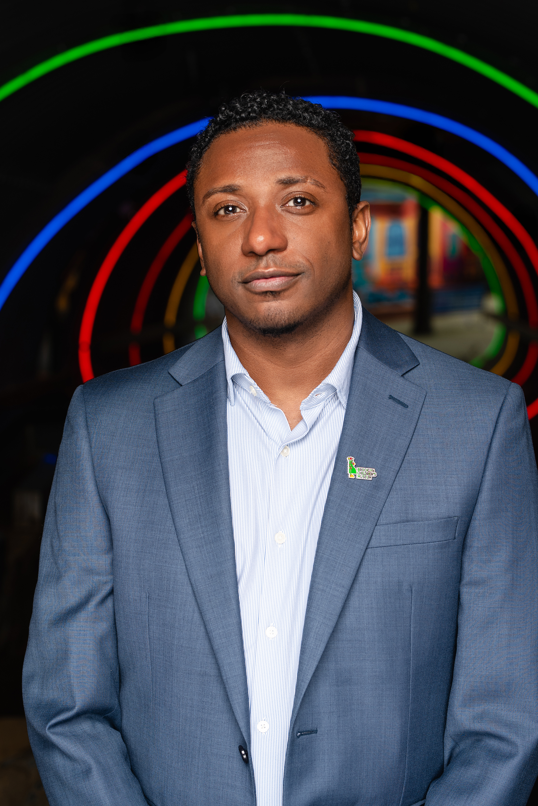 Professional portrait of a man in a blue suit against a dark backdrop with colorful rings