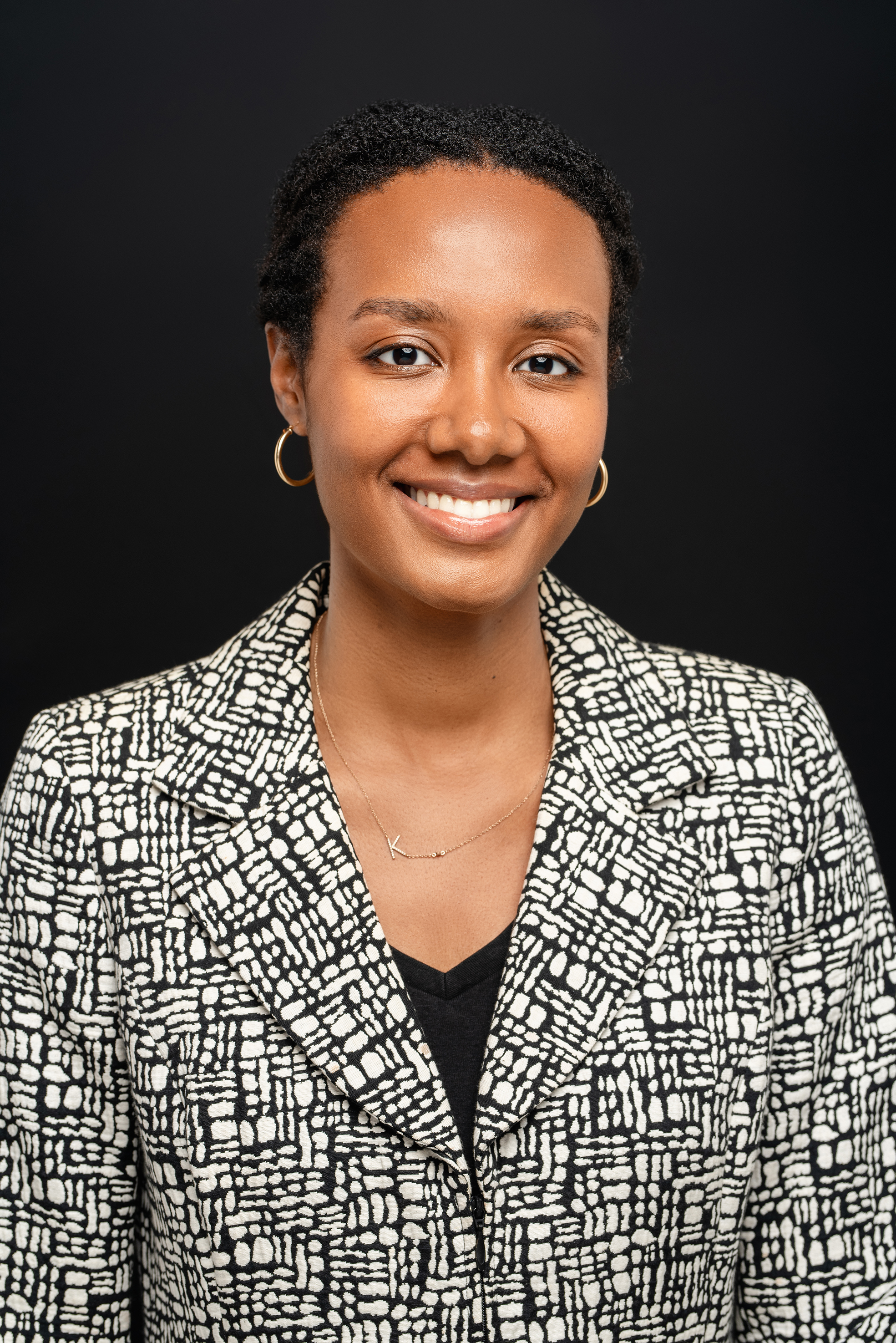 Professional portrait of a woman in a patterned blazer against a dark neutral background