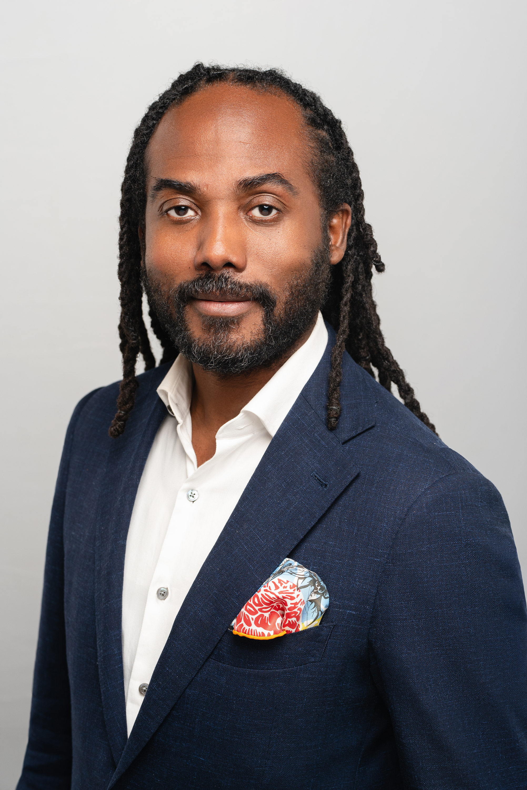 Professional portrait of a man in a navy suit against a light neutral background