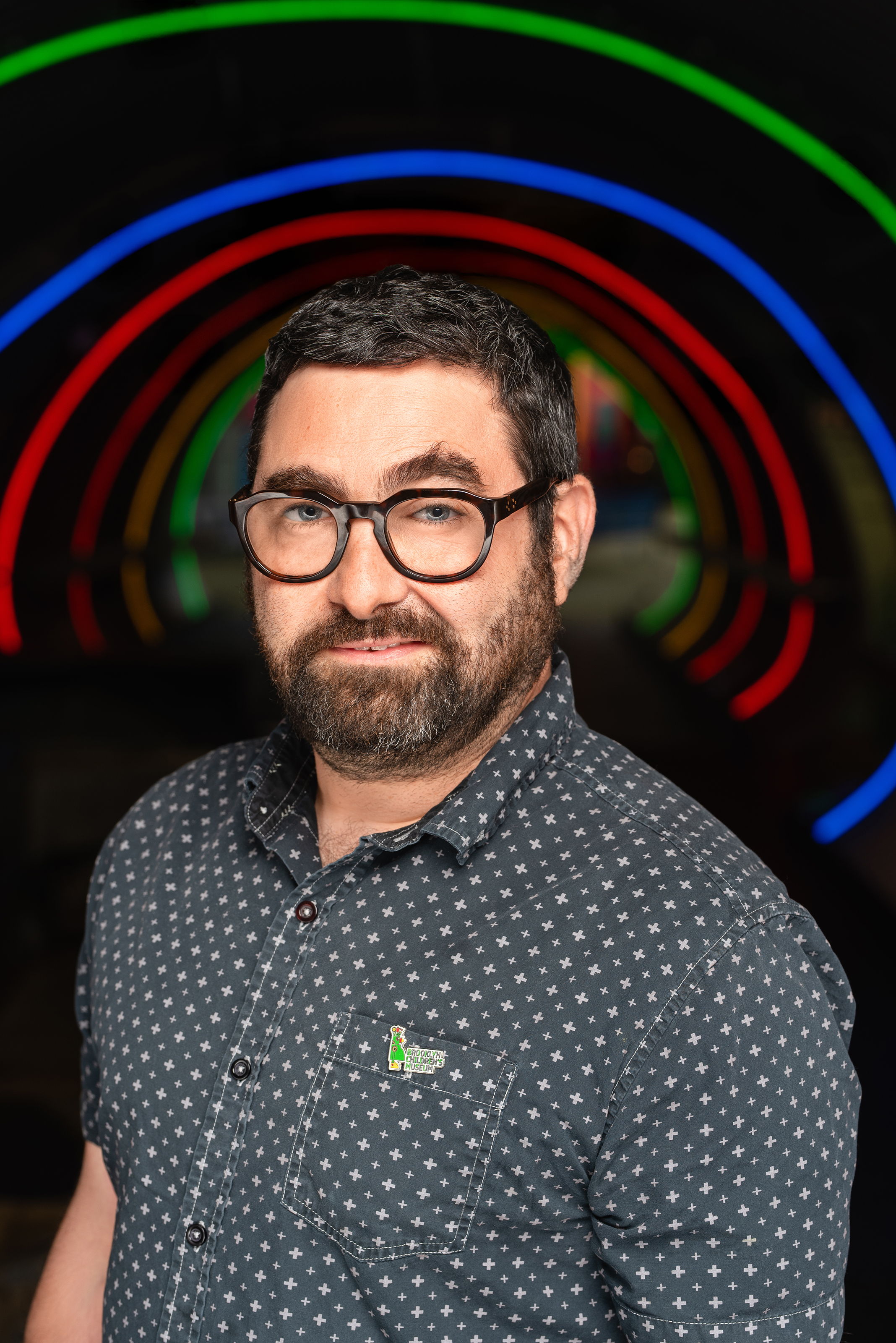Professional portrait of a man with glasses and a beard against a dark backdrop with colorful rings