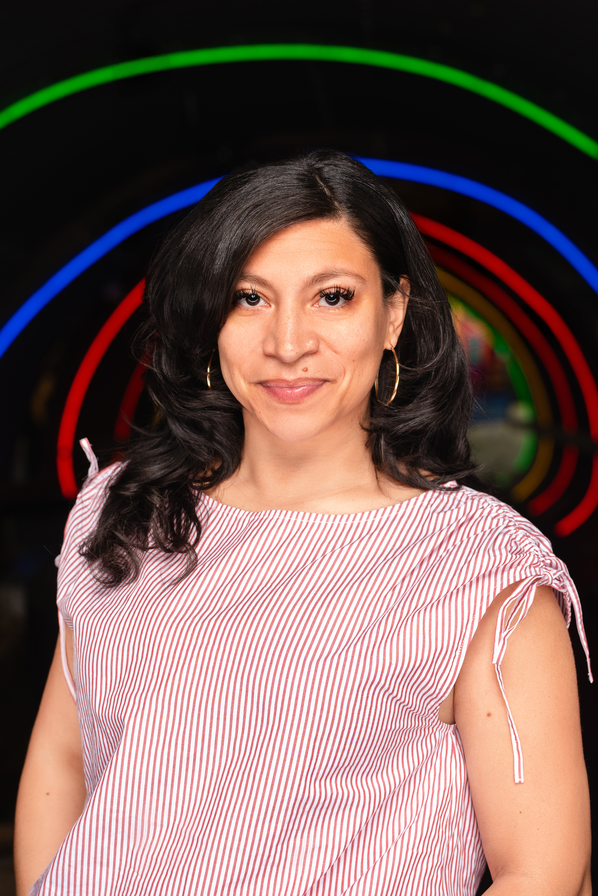 Professional portrait of a woman in a pink top against a dark backdrop with colorful rings